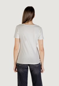T-shirt slim-fit beige chiaro, maniche corte, colletto tondo, tessuto in cotone morbido, schiena senza cuciture, texture liscia, abbinato a pantaloni in denim scuro.