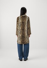 Leopardi mustriga kunstkarusnahast jakk pehme tekstuuriga, millel on krae ja pikad varrukad, koos vabalt istuvate siniste teksadega.