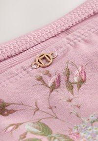 Gros plan sur un tissu rose imprimé floral avec un petit logo métallique rond doré attaché près d'une couture texturée.