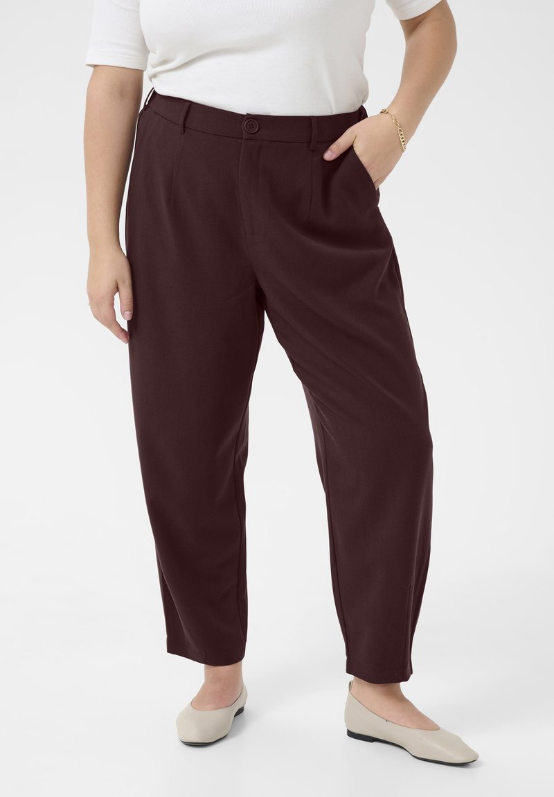 Maroon pleated trousers with a button closure, side pockets, and a relaxed fit. Paired with light-colored flats for a complete look.