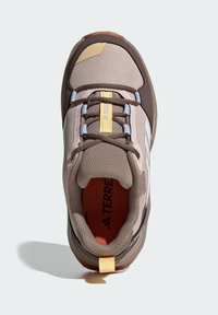 Světlé hnědé turistické boty s texturovaným svrškem, modrými a žlutými akcenty a gumovou podrážkou. Mají polstrovaný límec a viditelné logo.