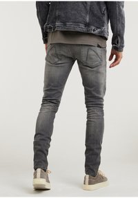 Jeans de mezclilla gris con un corte ajustado, que presentan una textura desgastada, bolsillos tipo parche y un diseño trasero limpio. Combinados con zapatillas grises.