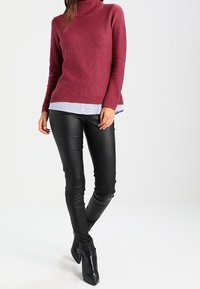 Burgunderfärgad polotröja med ribbstickade manschetter, lager på lager över en ljusblå skjorta, tillsammans med svarta läderbyxor och klackade ankelstövlar.