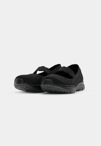 Black athletic shoes with a breathable knit upper, adjustable strap across the instep, and textured sole for grip. Rounded toe design.