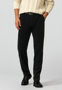 Schwarze Cordhose mit geradem Schnitt, verziert mit strukturierter Stoffoberfläche und standardmäßigen Gürtelschlaufen. Kombiniert mit einem cremefarbenen, kabelgestrickten Pullover.