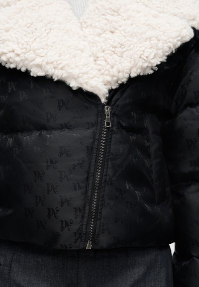 Μαύρο μπουφάν με μοτίβο, ασημένιο φερμουάρ και λευκό υφασμάτινο γιακά από shearling, φορεμένο πάνω από μπλε τζιν.