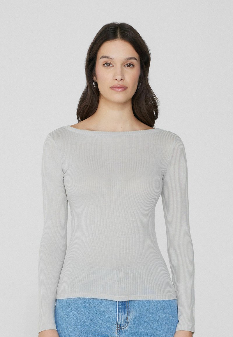 T-shirt long à manches gris clair à col bateau. Texture douce et coupe ajustée, associé à un jean en denim bleu.