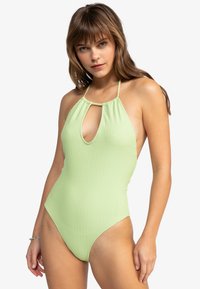 Maillot de bain une pièce vert à rayures avec colhalter, découpe en forme de clé et couverture minimale au niveau des hanches. Tissu texturé avec des fines bretelles.