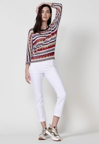 Pulover tricotat cu model zigzag multicolor, material ușor, guler rotund, asociat cu pantaloni albi cu manșete și pantofi sport bej.