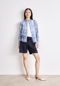 Light blue floral button-up shirt over a white top, paired with navy shorts and pale pink slingback heels. Simple, relaxed fit design.