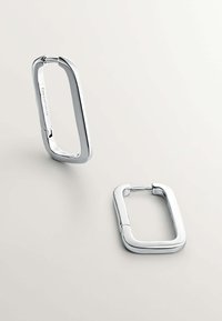 Pendientes de aro rectangulares de plata, con textura suave, superficie pulida y cierre de bisagra. Un fondo mate realza el brillo del accesorio.