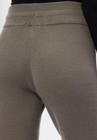 Rebraste, visoko strukirane tajice u prigušenoj maslinasto zelenoj boji. Mekani, elastični materijal s glatkom teksturom, s jednostavnim dizajnom struka.