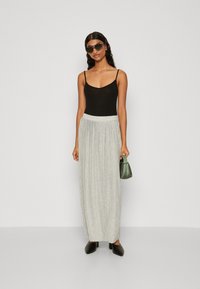 Svart tank topp, grå plissert maxi skjørt, svarte spisse mules, grønn veske og solbriller. Minimalistisk design med glatte teksturer.
