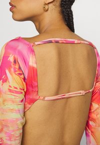 Langärmliges Oberteil mit einem lebhaften rosa und orangefarbenen abstrakten Muster, offener Rücken mit Riemenschlüssen und glatter Stoffstruktur.
