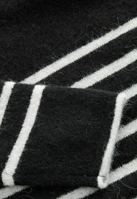 Schwarz-weißer gestreifter Wollstoff, der eine weiche Textur mit fusseligen Oberflächendetails zeigt. Die Streifen sind unregelmäßig angeordnet und deutlich voneinander abgegrenzt.