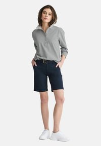 Grå långärmad tröja med krage och knappar, i kombination med marinblå shorts. Vita sneakers fulländar outfiten och framhäver en avslappnad stil.