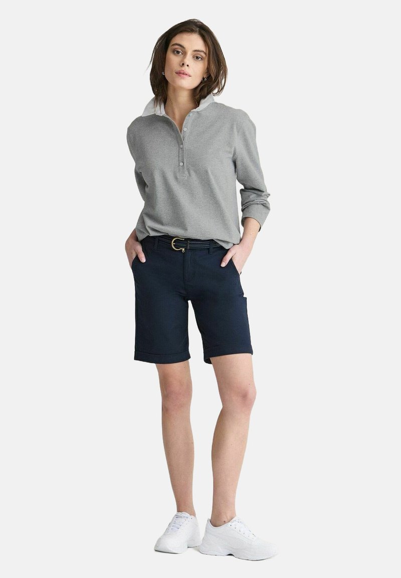 Grå långärmad tröja med krage och knappar, i kombination med marinblå shorts. Vita sneakers fulländar outfiten och framhäver en avslappnad stil.