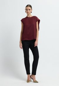 Top in satin bordeaux con maniche corte, con dettaglio di bottoni sul lato, abbinato a pantaloni neri slim fit e scarpe con tacco color taupe.