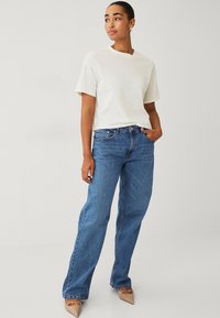 T-shirt crème à manches courtes associé à un jean droit en denim bleu. Les chaussures ont un bout pointu et une couleur beige clair. Design simple et moderne.