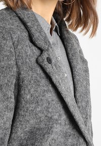 Grå uld-blandingsfrakke med en tekstureret overflade, notched revers og sorte knapper. Stoffet ser blødt ud og fremhæver en skræddersyet pasform.