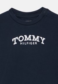 Tengerészkék kerek nyakú póló fehér "TOMMY HILFIGER" felirattal a mellkason, és patenttal a vállvarráson.