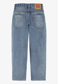 Jeans de mezclilla azul claro con un diseño de pierna recta, que cuentan con dos bolsillos traseros, un parche de marca de cuero y detalles de costura visibles.