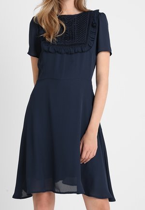 Vestido azul marino con mangas cortas, cuerpo texturizado que presenta volantes y costuras intrincadas, falda acampanada y tejido fluido.
