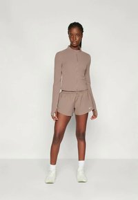 Kerge pruun sportlik lukuga ülemine osa ja sobivad lühikesed püksid, millel on lõdvas stiilis ja sujuv kangas. Lühikesed püksid kaunistab Nike logo.