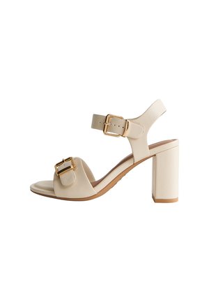 Sandaletto beige con tacco alto, open-toe, con due cinturini con fibbia dorata, uno alla caviglia e uno sopra le dita, e un tacco robusto.