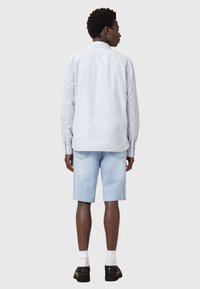 Chemise à rayures bleu clair à manches longues, portée avec un short en denim clair. Des chaussures noires et des chaussettes blanches complètent la tenue. Design simple et décontracté.
