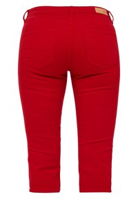 Punttihiuset punaisena, valmistettu puuvillasta, joissa on vartaloa myötäilevä malli, kaksi takataskua ja sileä pinta. Mukana nahkainen vyötunnus.