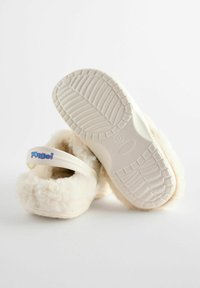 Chaussons couleur crème avec une texture duveteuse, une semelle en caoutchouc blanche et une sangle portant "Angel" en lettres bleues et roses.