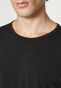 Schwarzes Rundhals-T-Shirt aus glattem Baumwollmaterial; Nahaufnahme, die den runden Ausschnitt und die weiche Textur hervorhebt. Keine Muster oder Akzente.