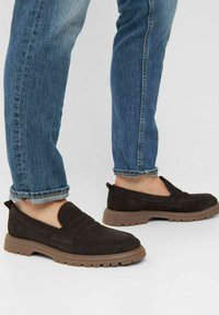 Braune Wildleder Slipper mit Gummisohle, ausgestattet mit einem vorderen Riemen und einem flachen Absatz, getragen mit hochgekrempelten blauen Jeans.