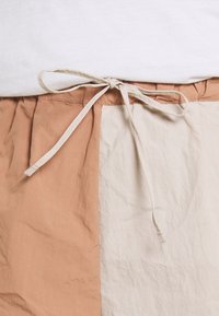 Ruskean ja kermaan sävyinen väriblokkihame, jossa on kerätty vyötärö ja beige kangasnauha. Materiaali näyttää kevyeltä ja teksturoidulta.