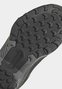 Semelle de chaussure en caoutchouc noir avec un design texturé. Caractéristiques des crampons hexagonaux profonds pour l'adhérence et une étiquette de marque centrale "TRAXION."