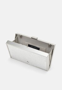 Stříbrná kabelka s texturovaným vnějším povrchem, uzavírání na klip a béžovou podšívkou s vnitřním štítkem. Kompaktní, obdélníkový tvar.