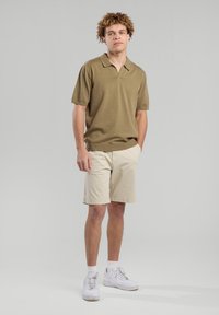 Khaki short-sleeve polo shirt with a collar, paired with beige shorts. The outfit is completed with white sneakers and a smooth texture.