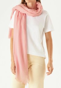 Écharpe rose clair en tissu doux, ornée d'une délicate broderie florale et de bords frangés, portée sur un t-shirt blanc.
