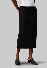 Black midi skirt with a straight cut, made of smooth fabric. Paired with pointed black mules, featuring a low heel and open back design.
