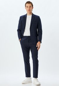Marineblauw geruit pak met een aansluitende blazer en taps toelopende broek, gecombineerd met een wit t-shirt en witte sneakers. Glad materiaal, modern ontwerp.