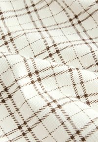 Tissu blanc avec un motif à carreaux marron comprenant des lignes pointillées croisées et de petits groupes de points aux intersections.
