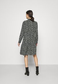 Vestido floral preto com mangas longas, cintura ajustada, saia até ao joelho, padrões de flores brancas, usado com botas de tornozelo de salto pretas.