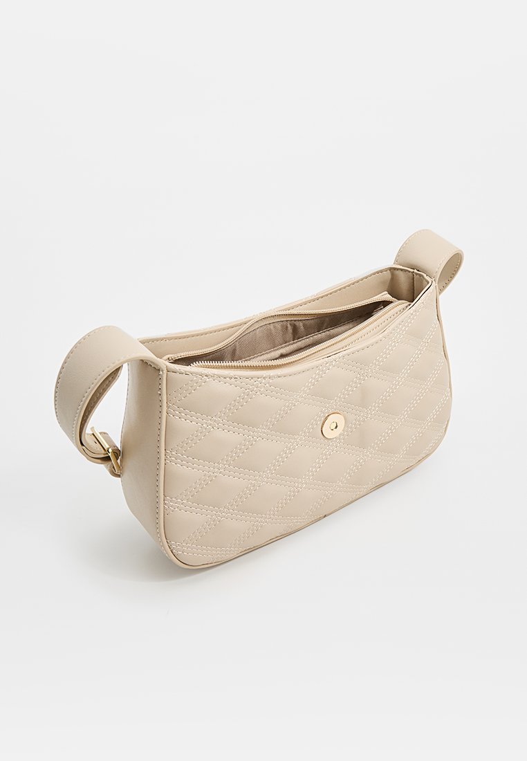 Beige gesteppte Handtasche mit glatter Textur, goldfarbenen Beschlägen, einem Reißverschluss und einem einzelnen Schulterriemen. Sie verfügt über ein Diamantmuster.