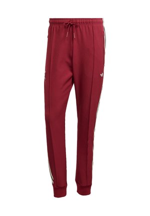Røde sweatpants med snor i taljen, sidelommer og sorte og hvide striber langs siderne. Lavet af et glat materiale.