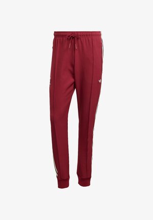 Røde sweatpants med snor i taljen, sidelommer og sorte og hvide striber langs siderne. Lavet af et glat materiale.