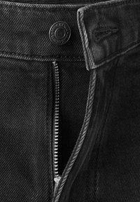 Czarne dżinsy z denimu z odpinanym metalowym zamkiem błyskawicznym i zatrzaskiem z guzikami oznaczonymi "KING DENIM" na pasku talii.