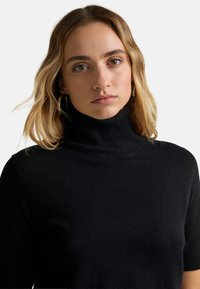 Černý rolák z měkké pleteniny, který má přiléhavý střih, krátké rukávy a vysoký límec.