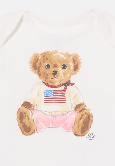 Meškiuko iliustracija ant balto bodžio; meškiukas turi rudus plaukus, dėvi megztinį su Amerikos vėliava ir rožinius kelnes su raudonu kaklaraiščiu.