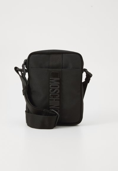 Sac bandoulière noir compact avec une sangle réglable et un logo MOSCHINO vertical au centre du panneau avant, sur fond blanc.